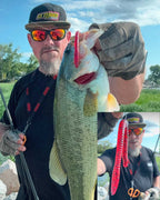 Matt Koser outdoors holds up a largemouth bass while wearing a black cap with a yellow and green 'GetUglyFishing!' logo, orange mirrored sunglasses, a black shirt, and gloves. A red segmented Culprit T-Rex lure hangs from the fish's mouth.