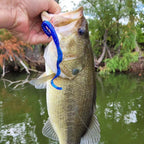 Snappfishing holds a largemouth bass outdoors over green water, with a Electric Blue Culprit Original worm soft plastic fishing lure visible in the fish's mouth.