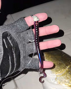 Sawyer Martin holds a fishing lure being held on a line over a fish, with a gloved hand visible. The Culprit Original Worm lure has a silver top, a dark purple segmented body with iridescent blue-purple highlights, and a hook at the bottom.