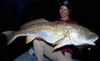 A smiling Sawyer Martin in a boat at night holds a very large redfish with both hands. The fish has a silvery back with golden-yellow sides and yellow fins.