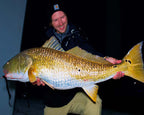 Sawyer Martin in a black beanie and dark jacket holds a very large redfish against a dark nighttime background.